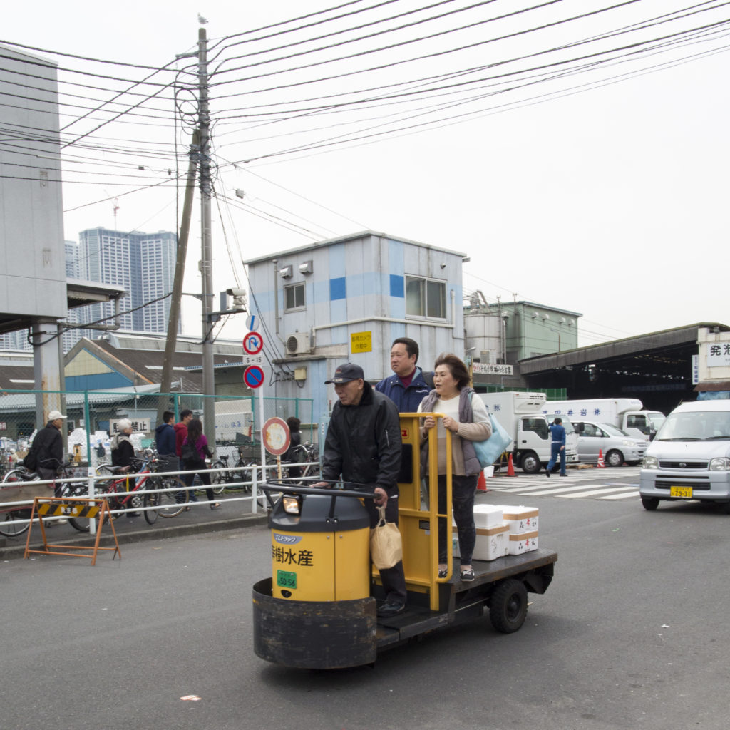 A fish market worker transports two people on a turret cart